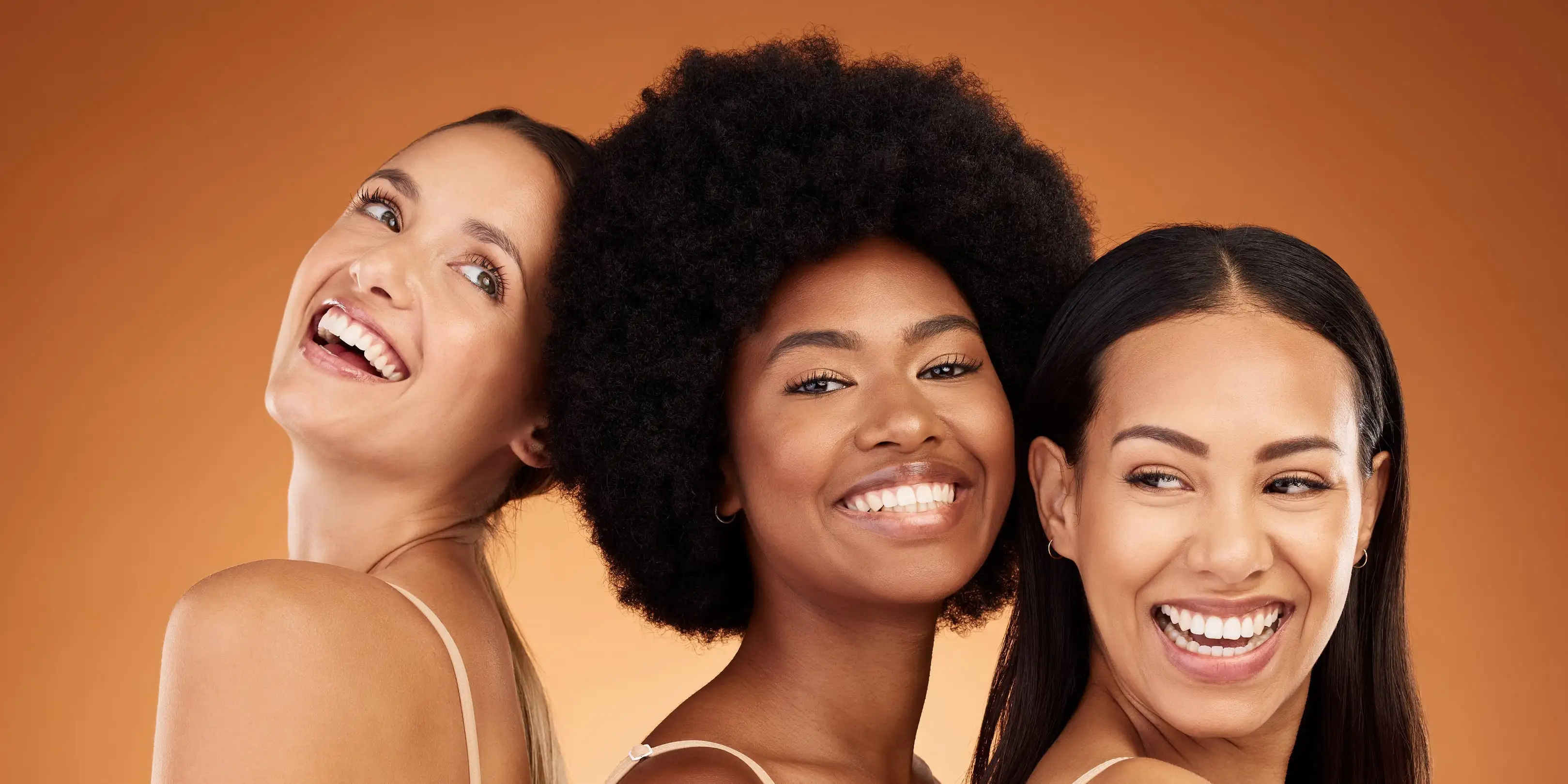 Three smiling women standing close together against a warm studio background
