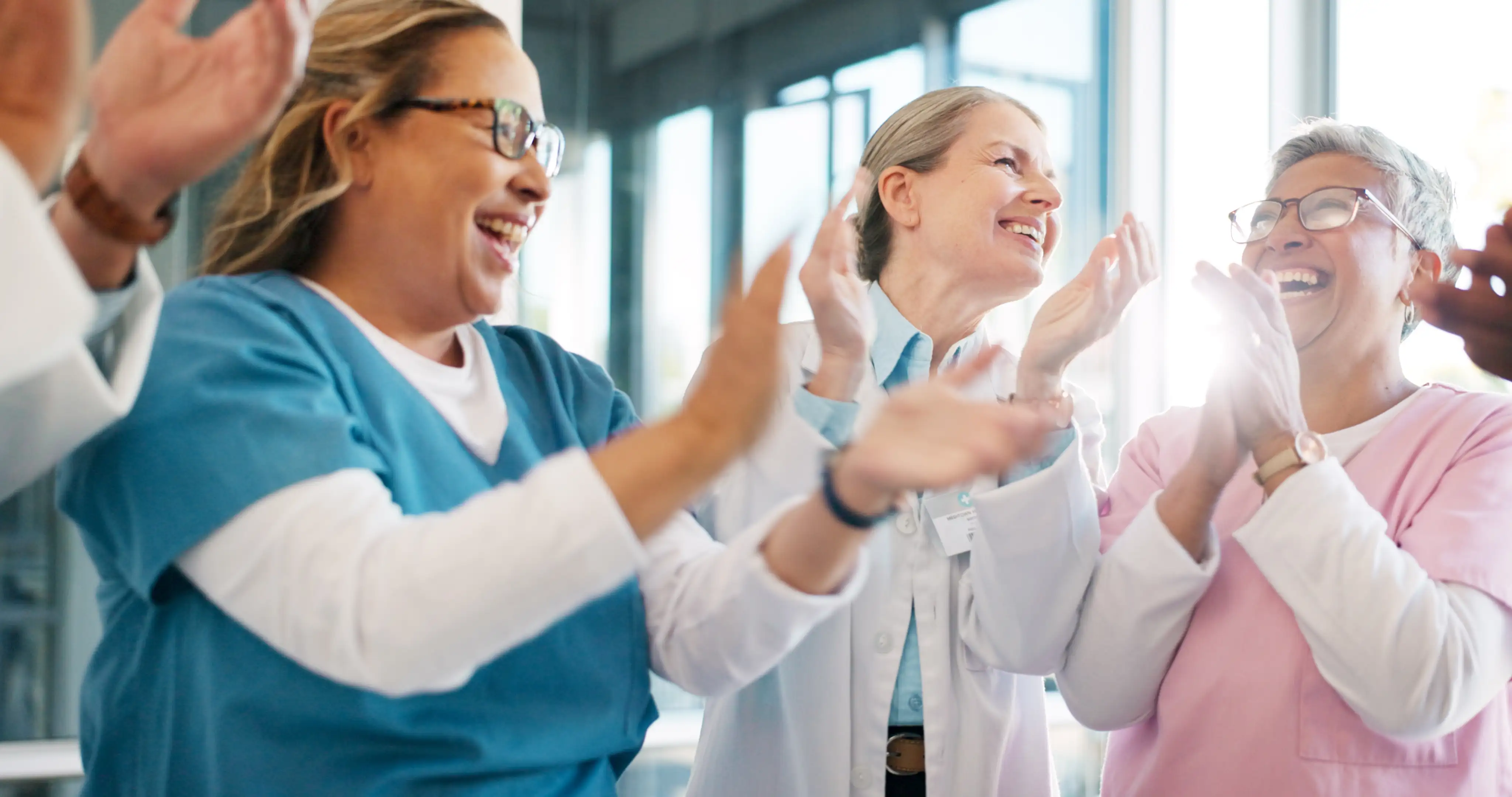 A group of healthcare professionals applauding together in a bright, window-lit room