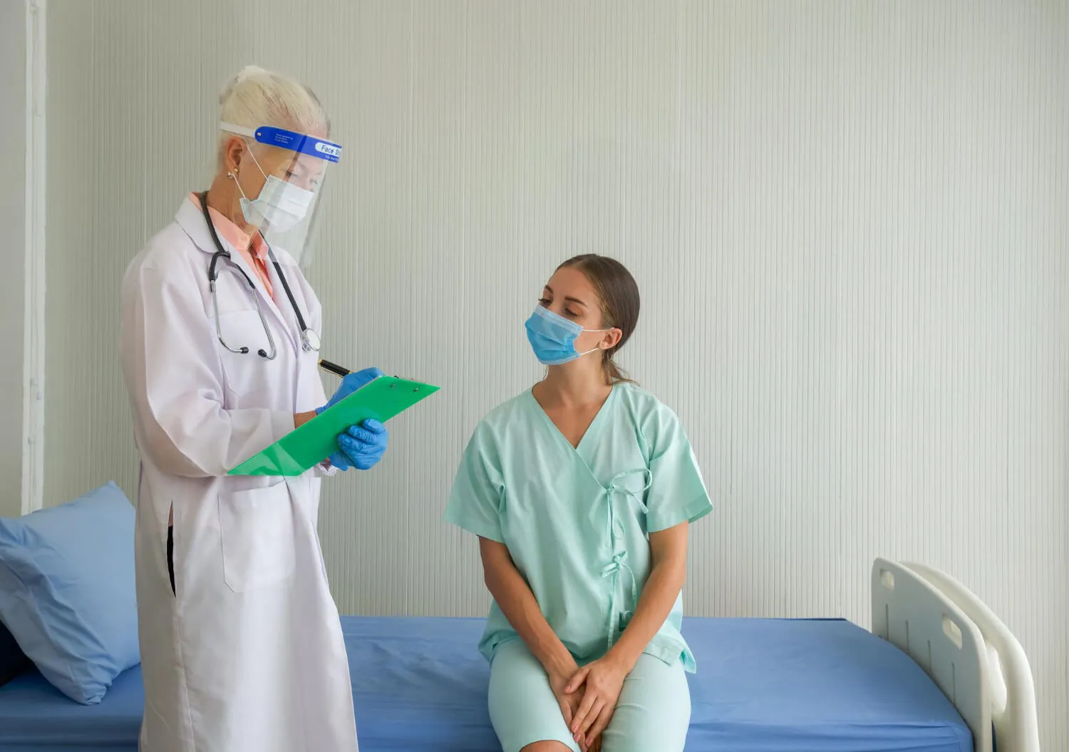 Doctor consulting with a patient in a hospital room while reviewing medical notes.