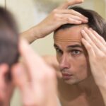 Man examining his hairline in the mirror while following hair transplant aftercare