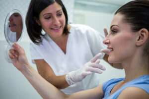 Woman holding a mirror while consulting with a female doctor about cosmetic treatment